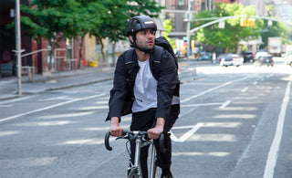 Cyclist wearing a black FEND Super collapsible helmet, riding a bike on an urban street in New York City.