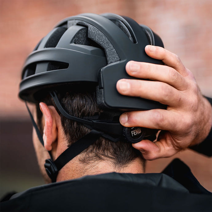 A man adjusts the fit of a FEND One helmet by turning the rear adjustment dial, showcasing its secure and customizable fit.