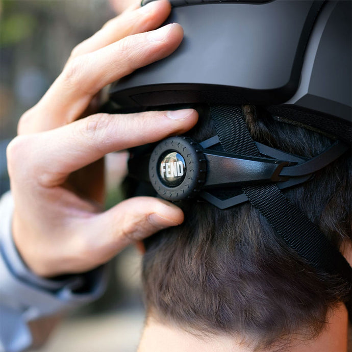 A man adjusting the fit of a black FEND Super helmet on his head using the back adjustment dial.