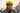 A man wearing a bright lime green bicycle helmet and sunglasses, standing outdoors on a city street with blurred buildings in the background.