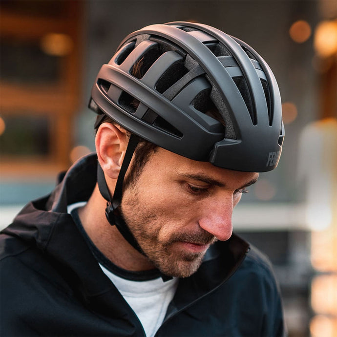 Man wearing a black matte FEND One folding city bike helmet, looking down, in a black jacket.