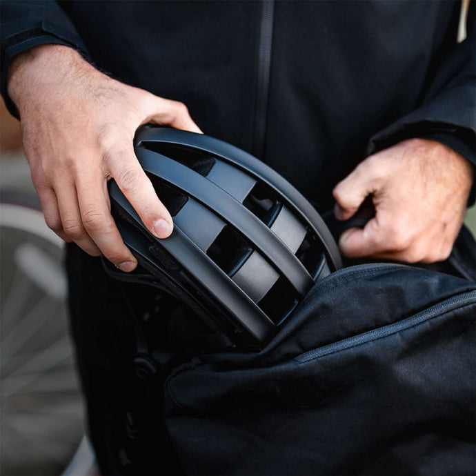 Man packing a lightweight collapsed black FEND One bike helmet into a backpack.