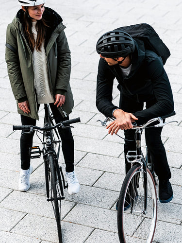 Urban commuters, man and woman, wearing FEND One folding bike helmets, standing with their bicycles on gray city tiles.