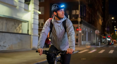 Urban commuter wearing black FEND Super folding bicycle helmet with ultra-bright lights, cycling in New York City at night.