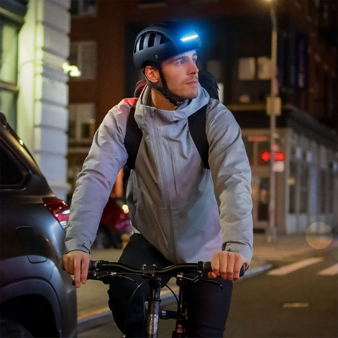 Urban commuter cycling in New York City at night wearing black FEND Super folding bicycle helmet with ultra-bright lights on.